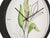 Reloj de pared con diseño de hoja verde sobre esfera blanca, manecillas negras