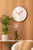 "Reloj de pared en la pared con esfera blanca y manecillas naranjas, borde plateado"