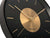 "Reloj de pared en detalle: esfera negra, manecillas doradas y centro redondo dorado"