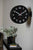 Reloj de pared en la pared con esfera negra, números blancos y manecillas rojas