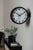 "Reloj de pared con borde negro, esfera blanca y segundero rojo"