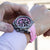 Reloj cronógrafo para hombre en la muñeca con correa de silicona rosa y esfera negra.