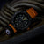 Pulsera de hombre con correa naranja y esfera oscura con detalles verdes