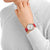 "Reloj de mujer con correa de cuero roja en la muñeca, esfera redonda blanca."