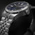 Pulsera de hombre primer plano: caja de acero inoxidable con corona y esfera azul, marcadores luminosos