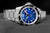 Reloj de buceo con esfera azul, manecillas rojas, bisel negro y pulsera de acero inoxidable