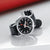 Reloj Mondaine Stop2Go inclinado: esfera negra, caja plateada, correa de cuero negra