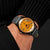 Reloj de pulsera para hombre en la muñeca: esfera naranja, correa de cuero gris con agujeros decorativos