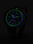 Reloj de hombre con esfera oscura y marcadores verdes luminosos, correa negra