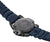 Vista trasera del reloj de hombre: correa azul, caja distintiva con grabado y soporte para la correa.