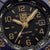 Primer plano de la esfera: reloj de hombre con manecillas doradas, ventana de fecha, índices luminosos y "200 Meters".