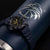 Reloj de hombre en la muñeca con correa azul oscuro, bisel con números y marcadores luminosos.