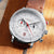Reloj de hombre, en diagonal: esfera blanca, correa de cuero marrón, agujas rojas, cronógrafo