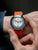 Pulsera de hombre en la muñeca con correa textil naranja y esfera multicolor
