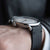 Reloj de hombre en la muñeca: correa de cuero negra, caja y corona plateadas.