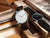 "Reloj de mujer con correa de cuero marrón, esfera blanca y manecilla azul"