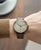 Reloj de hombre en la muñeca: correa de cuero marrón, esfera beige y caja de oro rosa.