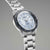 Vista lateral de reloj para hombre con caja de metal, esfera plateada y bisel azul