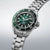 Reloj de hombre de perfil con esfera verde, caja de acero y marcadores en el bisel