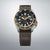 Reloj de hombre con esfera negra, bisel dorado y correa de cuero marrón.