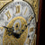 Esfera de reloj de pie con números romanos, adornos dorados y manecillas ennegrecidas