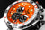 Reloj de pulsera para hombre en detalle: esfera naranja, subesferas negras, bisel plateado