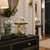 Reloj de mesa mecánico con campana de cristal, columnas doradas y base verde, esfera redonda