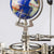 Detalle del mecanismo de reloj con engranaje de latón, varillas metálicas y remate de globo en azul