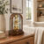 Reloj de mesa de madera sobre mesa de madera, arco de cristal, mecanismo de reloj dorado con números romanos