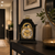 Reloj de mesa negro con indicador de fase lunar dorado sobre consola con marco decorativo