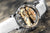 Primer plano de un reloj con movimiento dorado e índices plateados en la esfera