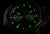 Pulsera de hombre con esfera oscura y marcadores luminosos verdes, parte de la caja de acero visible