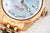 Vista de cerca de reloj de mujer: esfera azul, bisel dorado, indicador de fecha a las 5 en punto.