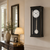 Reloj de pared con marco negro, esfera blanca y péndulo de cristal