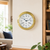 Reloj de pared con caja redonda de latón, esfera blanca y manecillas azules, marcadores romanos.
