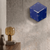 Reloj de pared en caja cúbica azul con números y manecillas blancos en la pared