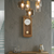 Reloj de pared de madera con esfera blanca, borde dorado y péndulo redondo.