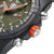 Detalle de reloj para hombre: caja negra con corona en naranja y botones metálicos en el lateral