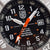 Reloj de hombre en primer plano: esfera negra con segundero naranja y ventana de fecha.