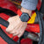 Imagen de muestra: reloj automático con correa de silicona roja en la muñeca sobre un objeto amarillo y rojo
