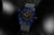 Reloj de pulsera para hombre sobre fondo negro: caja azul, brillo verde oscuro en la esfera y las manecillas.