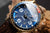 Reloj de hombre en detalle: esfera azul con manecillas luminosas, caja dorada