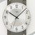 Nahaufnahme Wanduhr: rundes Ziffernblatt mit AMS-Logo, schwarzen Zeigern und Mineralglas