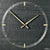 Nahaufnahme: runde Wanduhr aus Naturschiefer mit goldener Zeigerkreuzung und Strichindizes.