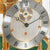 Esfera de reloj de mesa con números romanos, superficie plateada y manecillas doradas bajo cristal