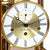 Primer plano del reloj de mesa: mecanismo dorado, esfera blanca con marcadores de hora romanos