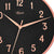 Primer plano de reloj de pared: esfera negra, manecillas de oro rosa y números romanos