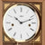 Esfera de reloj de pared con logo Hermle, marco dorado, números romanos, primer plano.